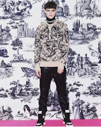 a man in a black sweater standing in front of a wallpaper