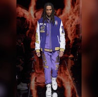 a man in a purple jacket walks down a runway